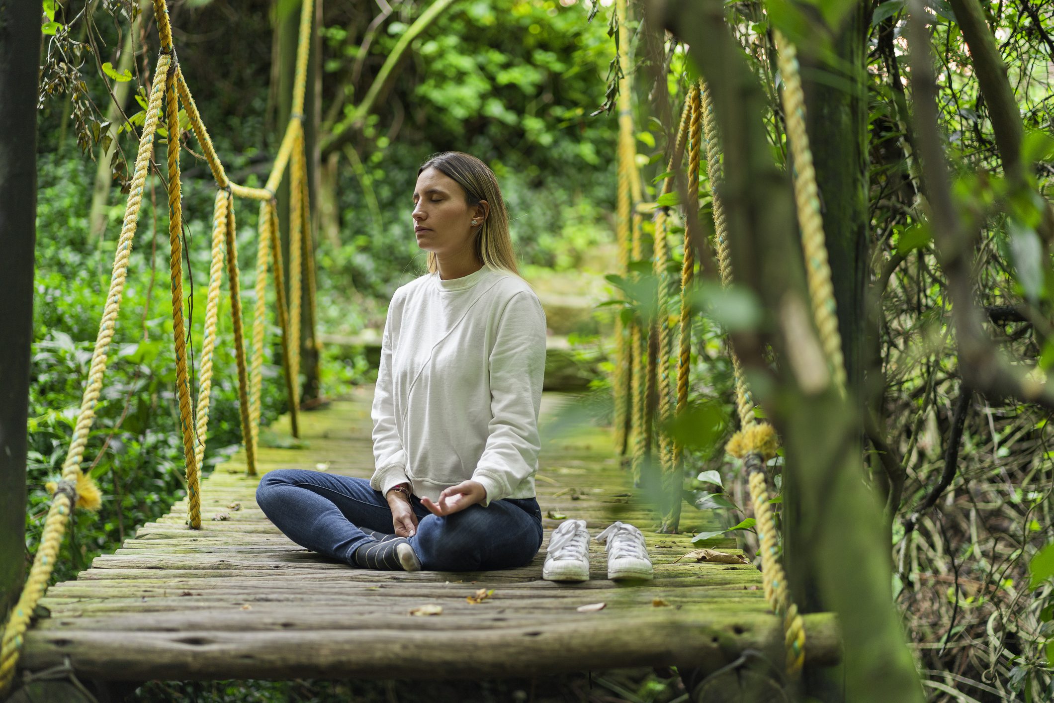 Latina woman from Bogota Colombia between 20 and 29 years old, sitting on the suspension bridge that she found in the forest while walking and decided to do meditation on it.